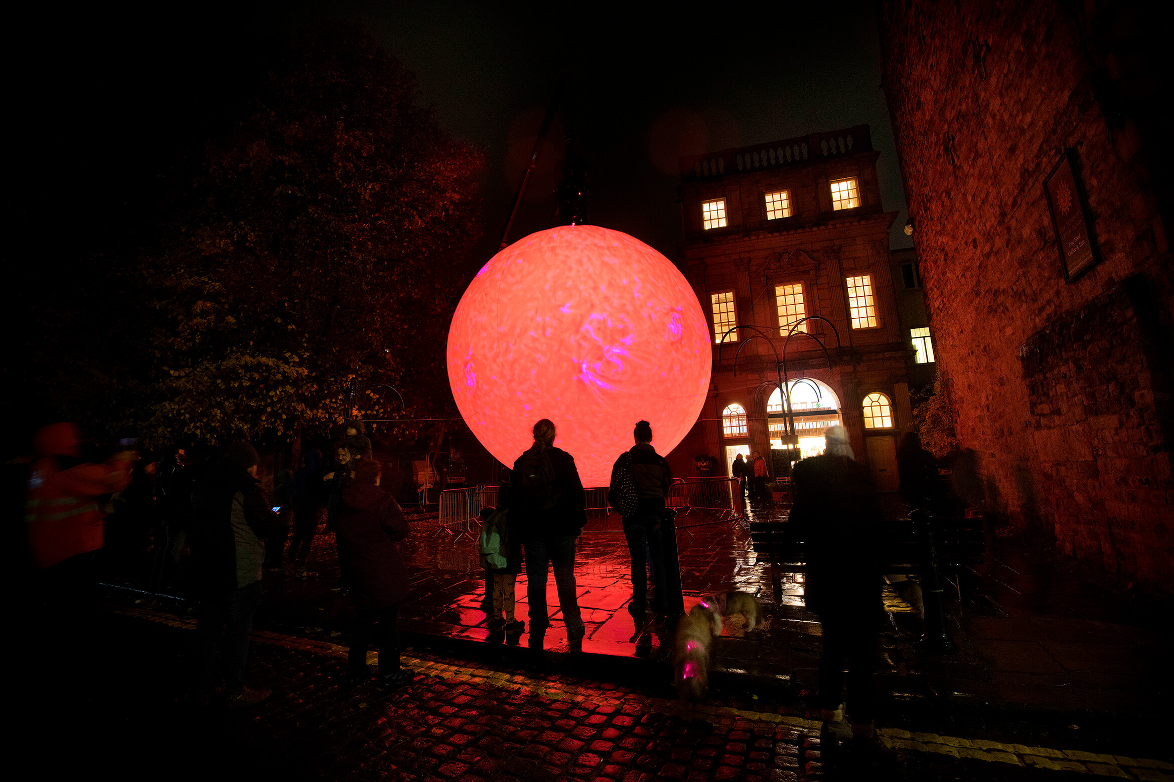 Photograph of SUN taken outside at night and showing in a group of people watching it during its red phase