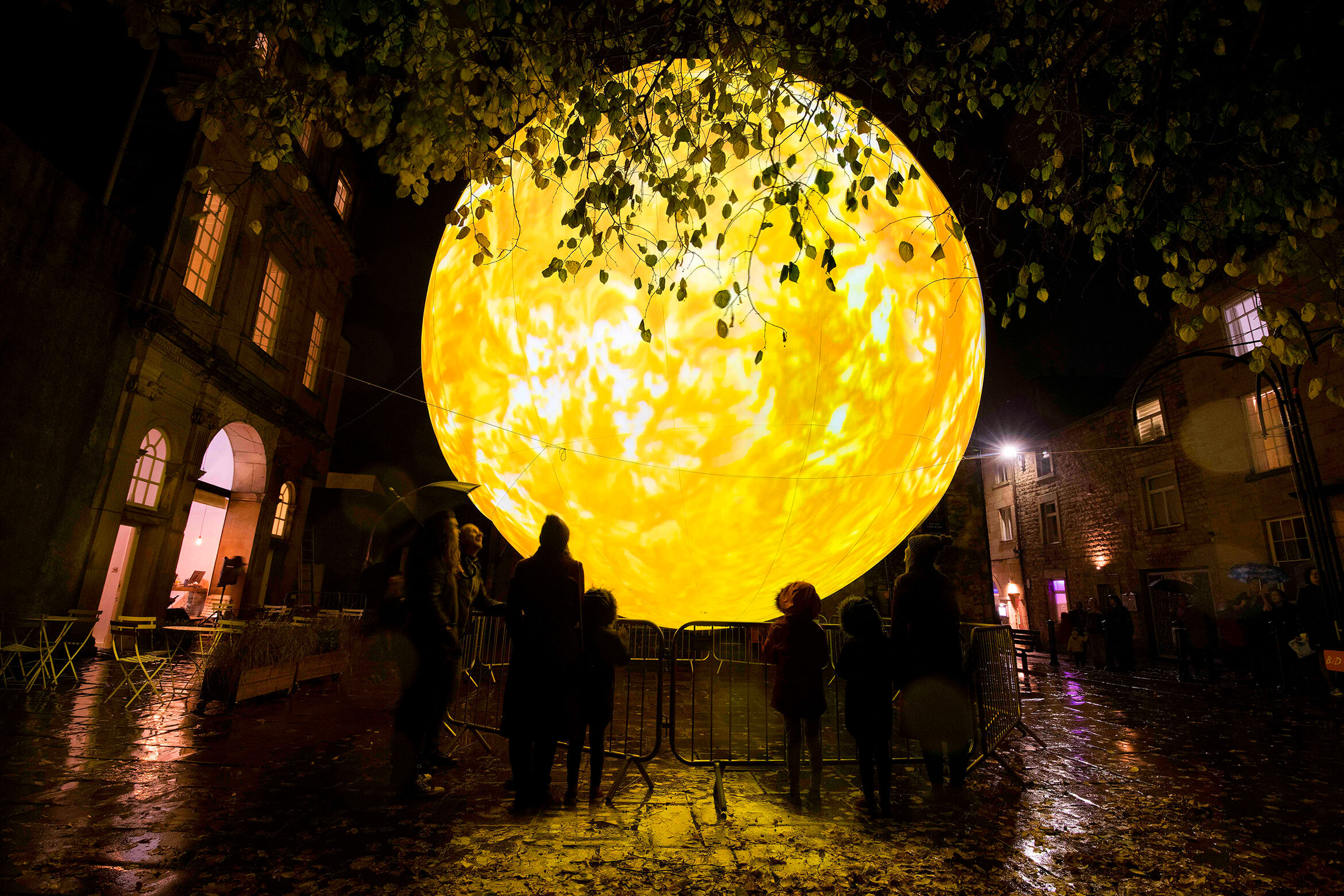 Photograph of SUN taken outside at night and showing in a group of people watching it during its yellow phase